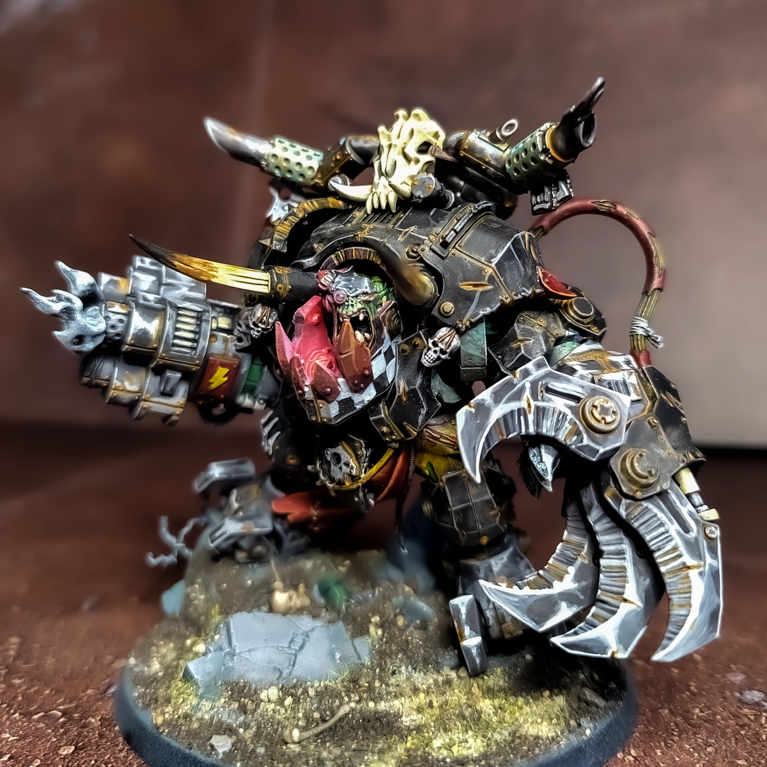 A photograph of a Ghazgkull Thraka model with non-metallic metal, rust and weathering effects, freehanded checkerboard pattern, and red object source lighting from below the head.
